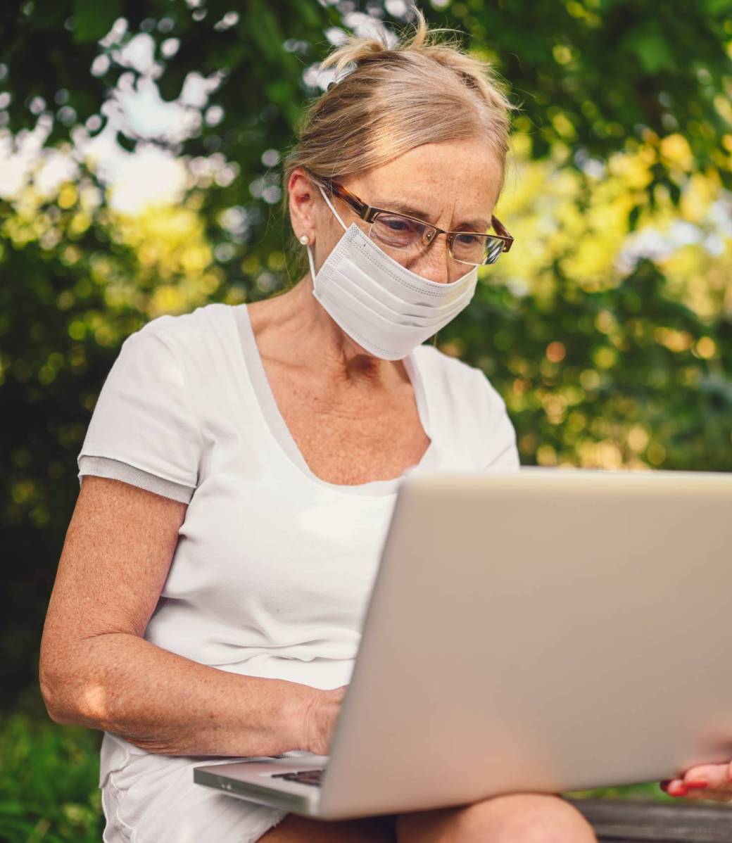 Technology, old age people concept - elderly senior old woman in face protective mask working online with laptop computer outdoor in the garden. Remote work, distance education.